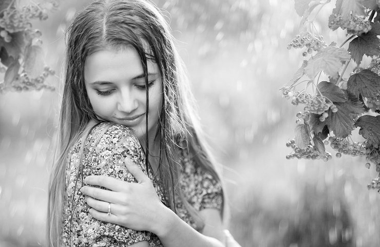 Young female with wet hair enjoying the rain and looking down, in summer garden, hugging yourself.Happy rainy day.
