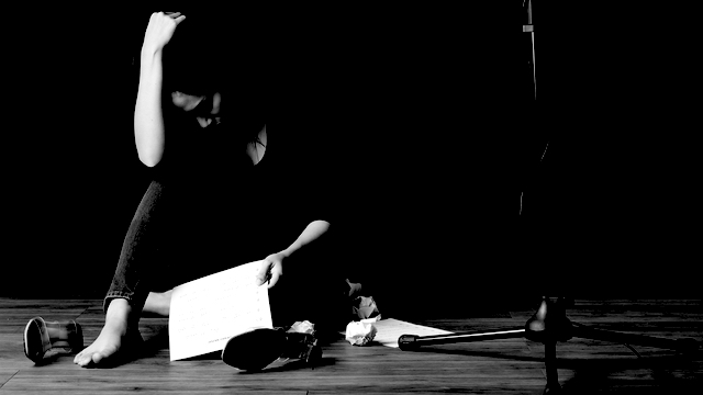 Female performer laying on the stage upset, her had on her hand, performance notes on the floor. 