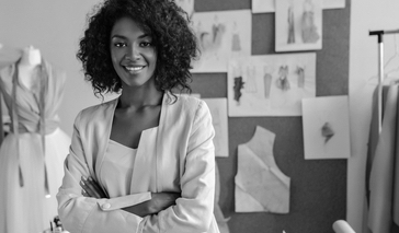 Female fashion designer poses in office, leans on table. 