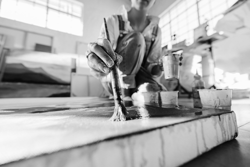 Female artist painting on a large canvas with a paintbrush, working on the floor of her art studio. 