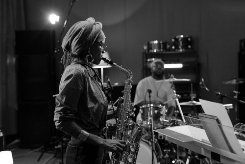 Musicians rehearsing jazz performance with saxophonist in foreground and drummer in background. 
