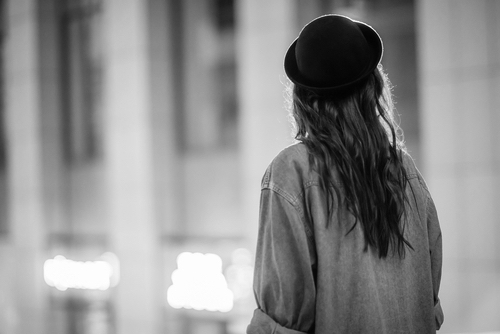 Back view of a stylish female tourist in black hat. The girl walks on a night city, exploring the world 