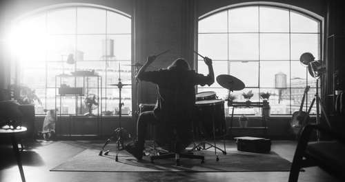 Male with Long Hair Sitting with Their Back to Camera, Playing Drum Solo Alone.