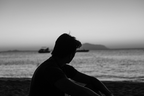 A man sits against the backdrop of sunset on the beach. Serene Sunset Reflection by the Beach