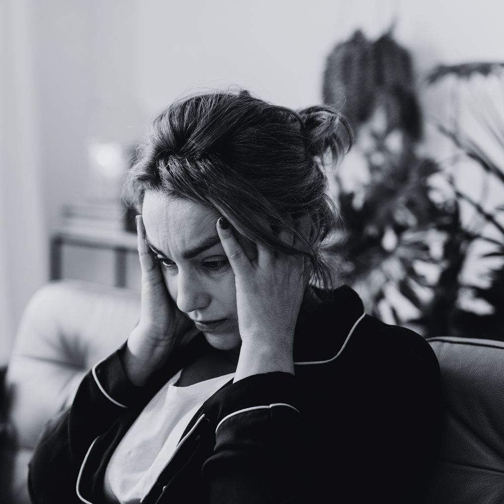 Woman sitting on couch holding head in anxiety