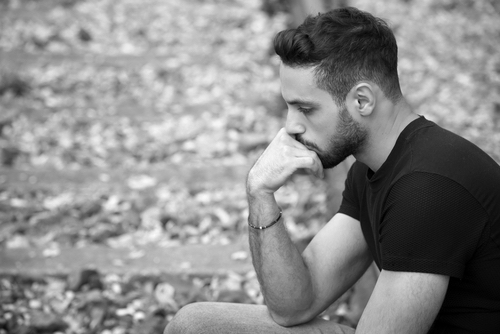 handsome young man sitting outside on train tracks and looking pensive