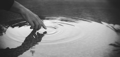 Man hand touching the water with his finger, creating water ripples 