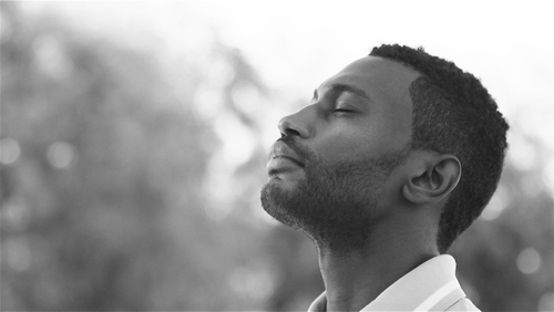 A man enjoys a serene moment in a park, breathing deeply amidst greenery.