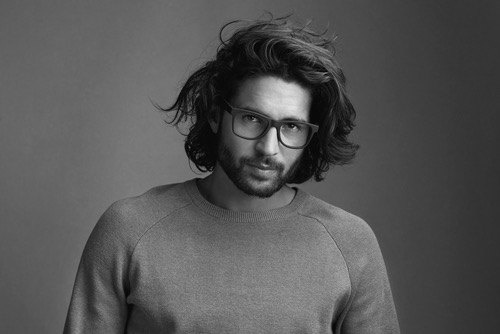 Man portrait, steady, vulnerable gaze, messy hair, with glasses, in sweater - mirrors of inner world of a senile creative man. 