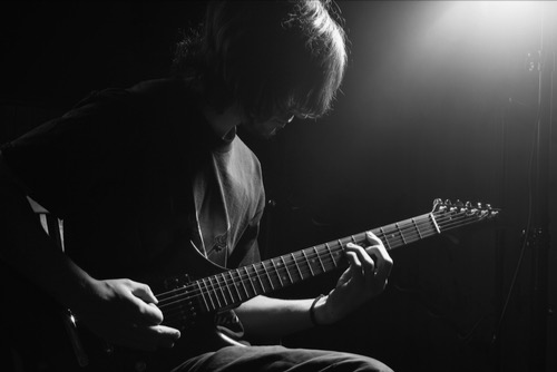 Musician, alone playing his guitar, dark environment with a ray of hope 