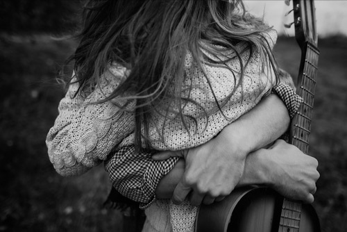 Man holding a guitar and and with a warm and strong embrace of a female: representing safety, intimate connection, and creativity.