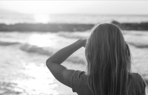 Female, back view, long hair, watching the sunset at the beach. Image go hope and possibilities.