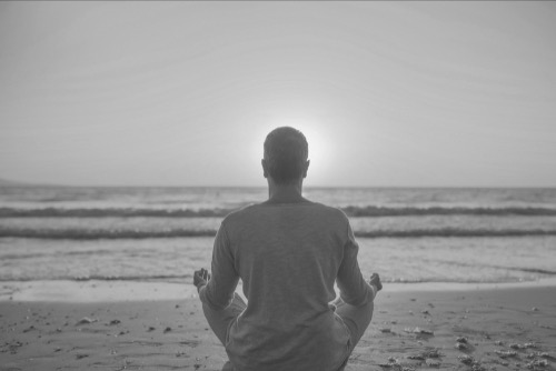 Man meditating at the beach, the sun up, in the middle of ocean - image of healing and hope 