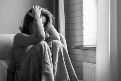 Female, holding her head in her arms, by the window, tired and overhelmed