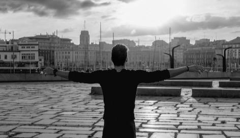 Man, back view, arms wide up, watching the sixty, sunrise bright in the horizon, image of healing and hope.