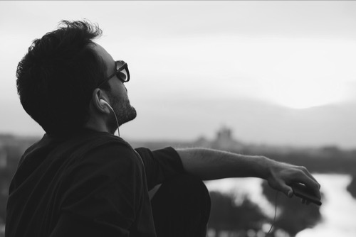 Man alone, listenin on the phone with headsets - he is looking up: image of loneliness, being with his world, but also image of hope for healing.