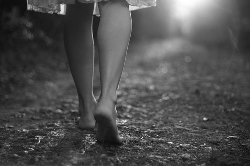 Female bare feet walking earth, sun ray coming through ahead of her path; metaphor of venerability, authenticity, groundedness, embodiment, and possibilities.