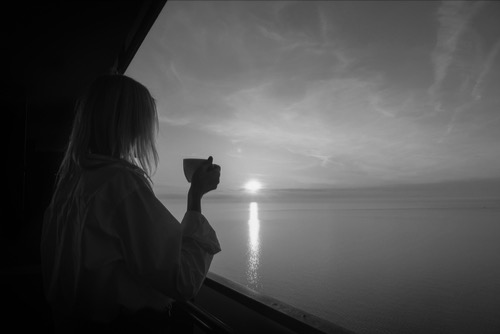 Female, holding a cup of tea, watching the sunrise, of the ocean from her balcony. Image of healing and hope.