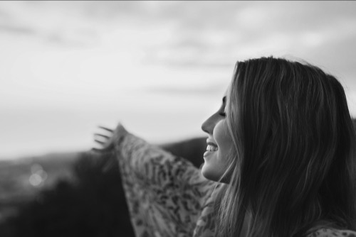 Female smiling, side image, pointing her hand to the world. Image of healing, hope, new possibilities. 