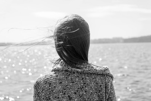 Female, watching the horizon at the beach, back view, long hair flowing in the wind. Image of being on the way to emotional freedom from trauma.